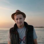 Portrait of a young man with a hat enjoying the serene beach sunset.