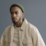 Portrait of an African American man wearing a green beanie and beige jacket in a studio setting.